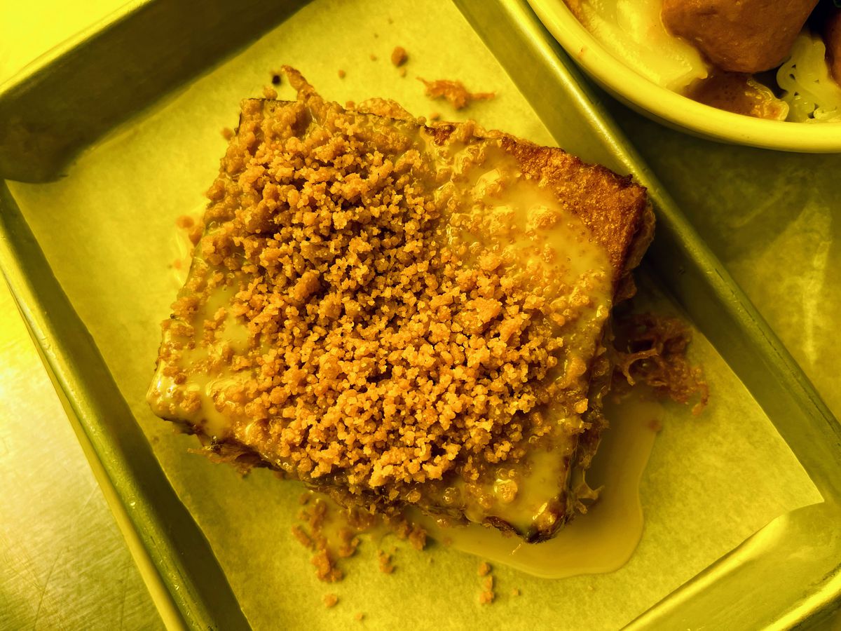 An overhead shot of a cube of bread stuffed with salted egg yolk and topped with a condensed milk sauce and sweet crumble.