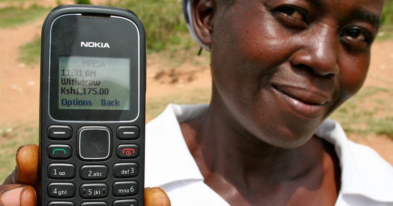 A smiling person holds up their cellphone to show the money transaction on its screen.