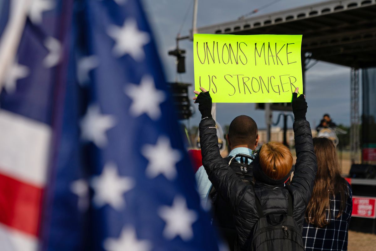 A person at a rally holds up a sign that reads “unions make us stronger.”