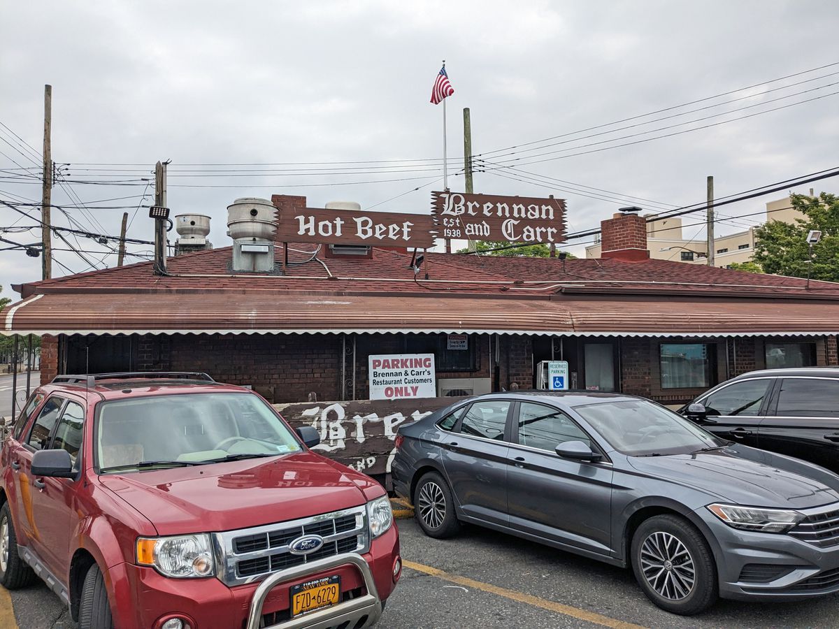 A long low building with a parking lot in front and a sign that says hot beef.
