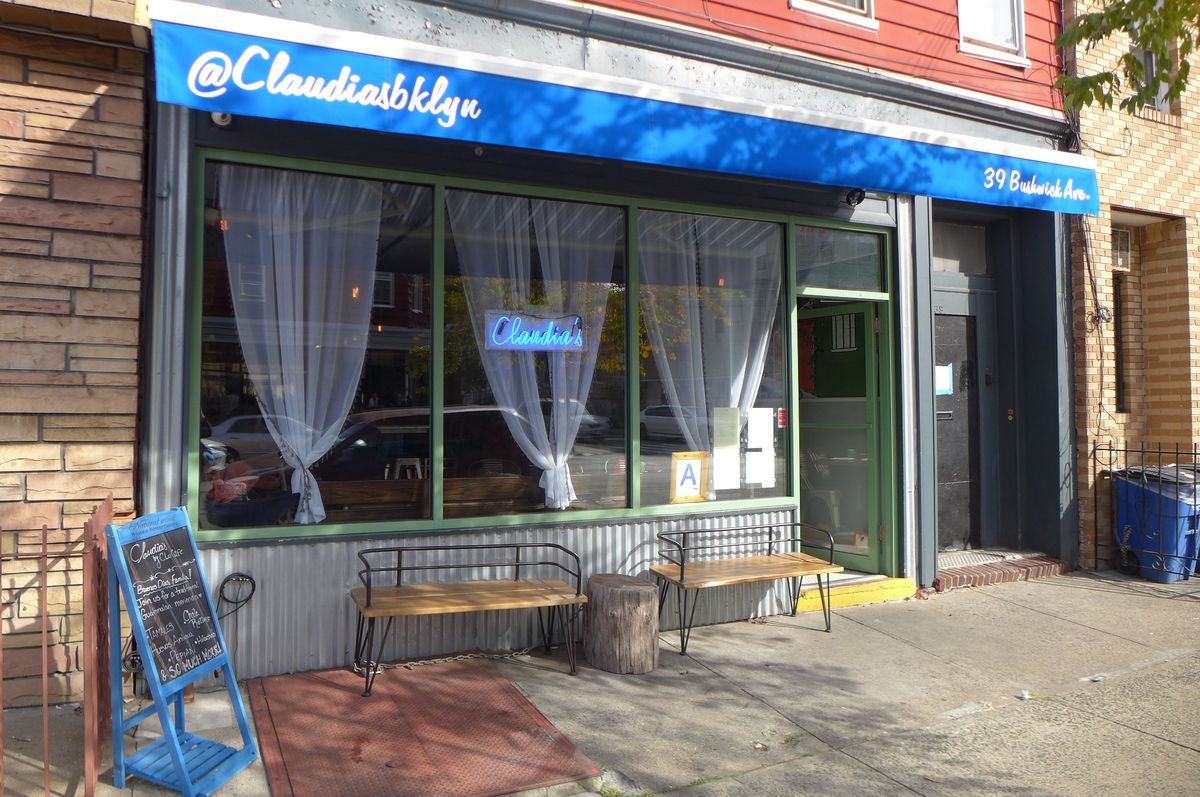 A storefront with a blue awning and blue neon in the window reading Claudia’s.