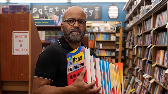 A bald man with glasses and a beard holding a stack of books in a book store.