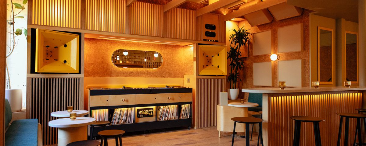 A wood paneled room is filled with records and small tables with black barstools.