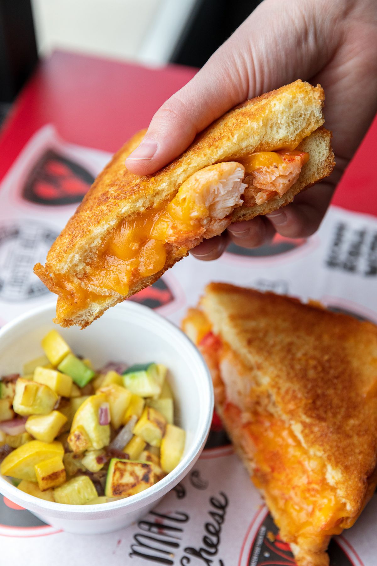 A hand holds half of a lobster grilled cheese.