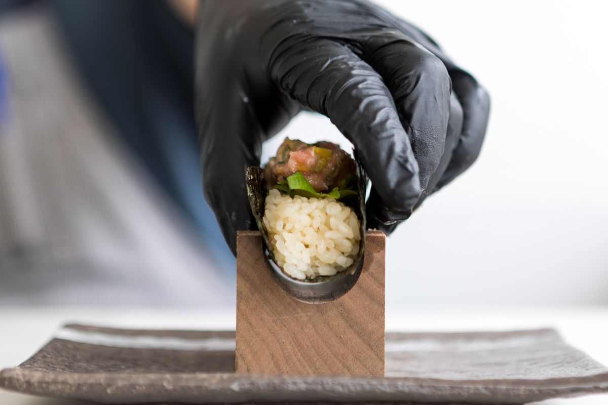 A chef places a handroll into a wooden holder.