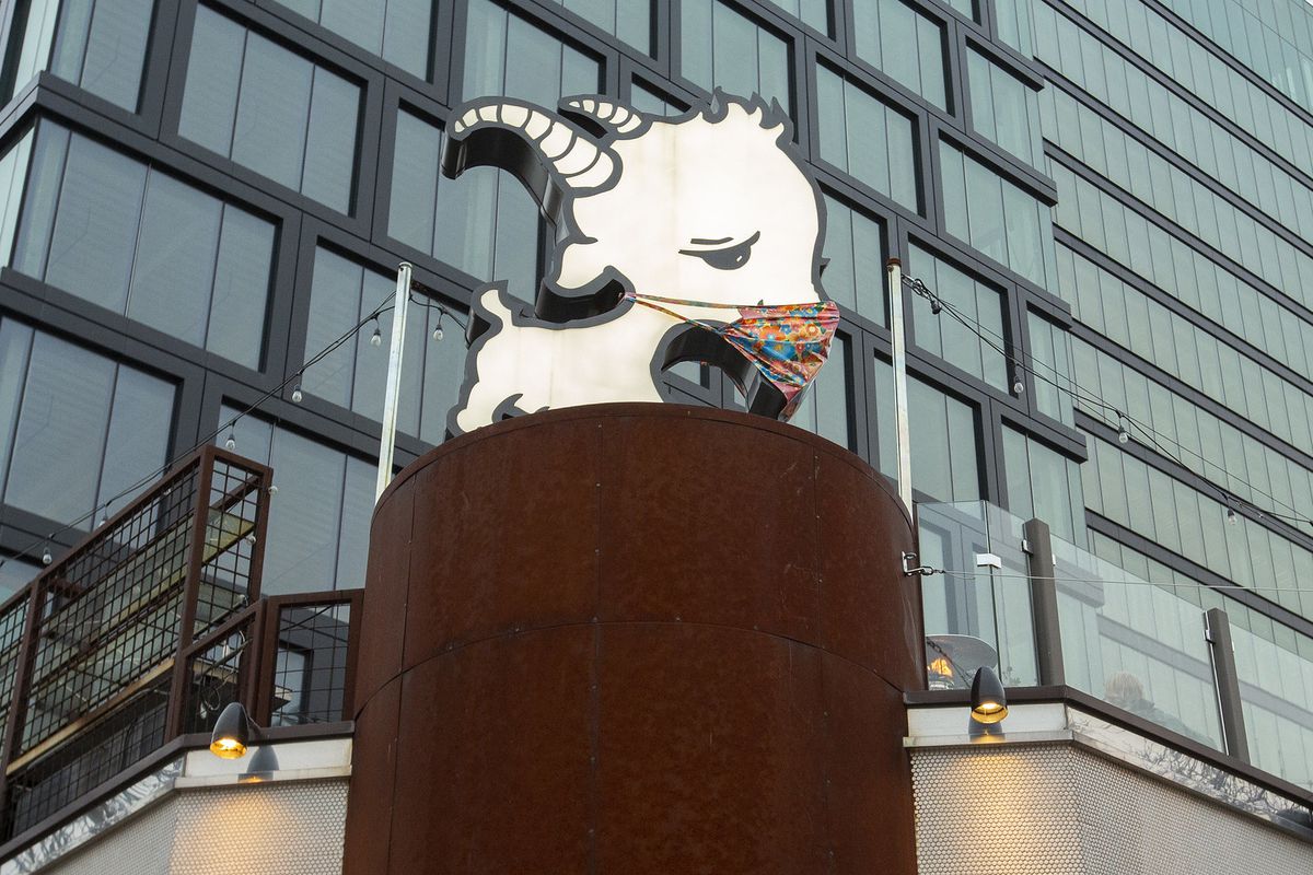 A cartoonish goat sign with a mask over it on the roof of a restaurant.