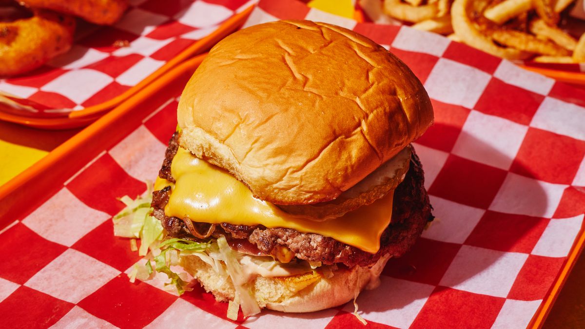 A double smash burger topped with melty cheese on a Martin’s Potato Roll sits on red-and-white checkered paper.