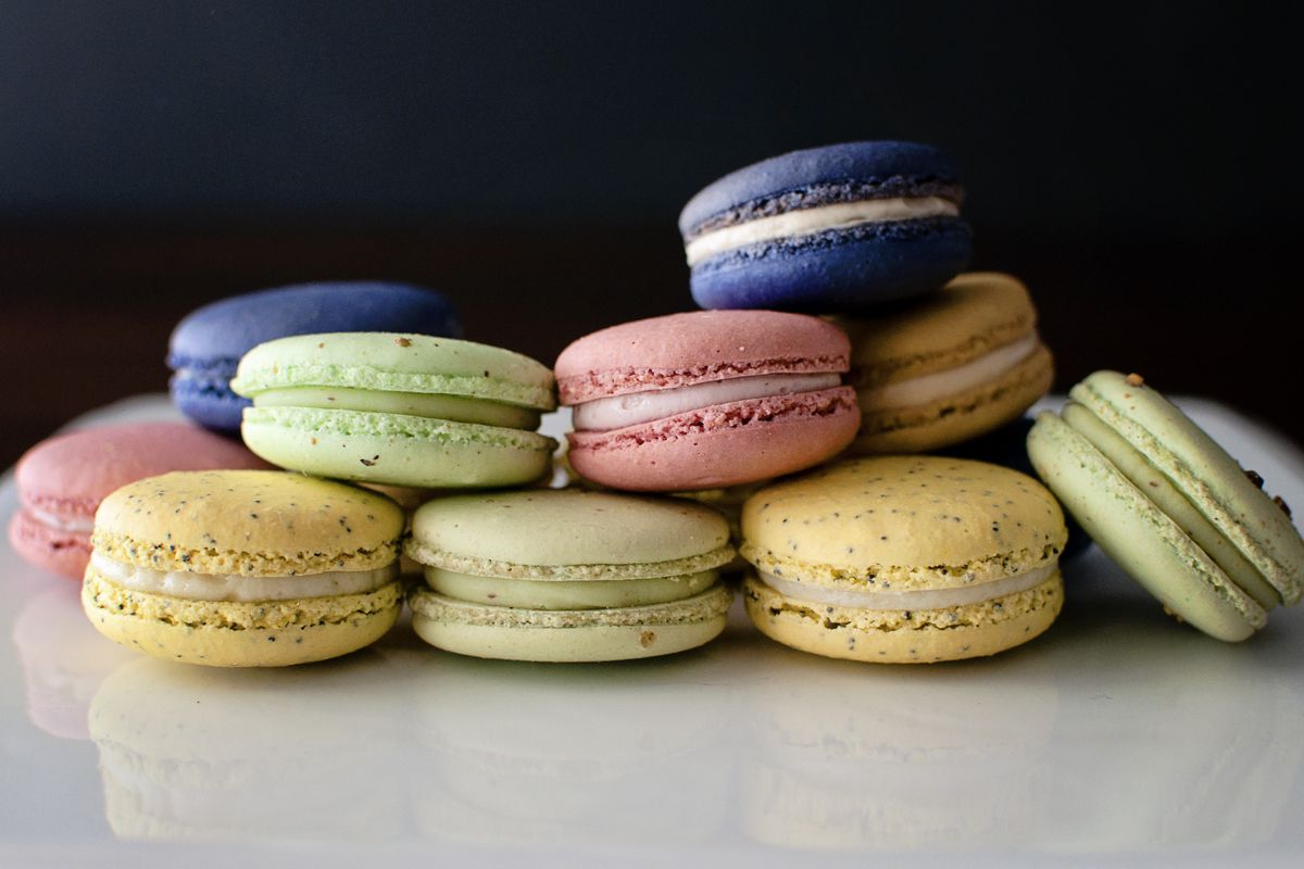 Pink, yellow, blue, and green macarons stacked on a shiny white reflective countertop with a dark background