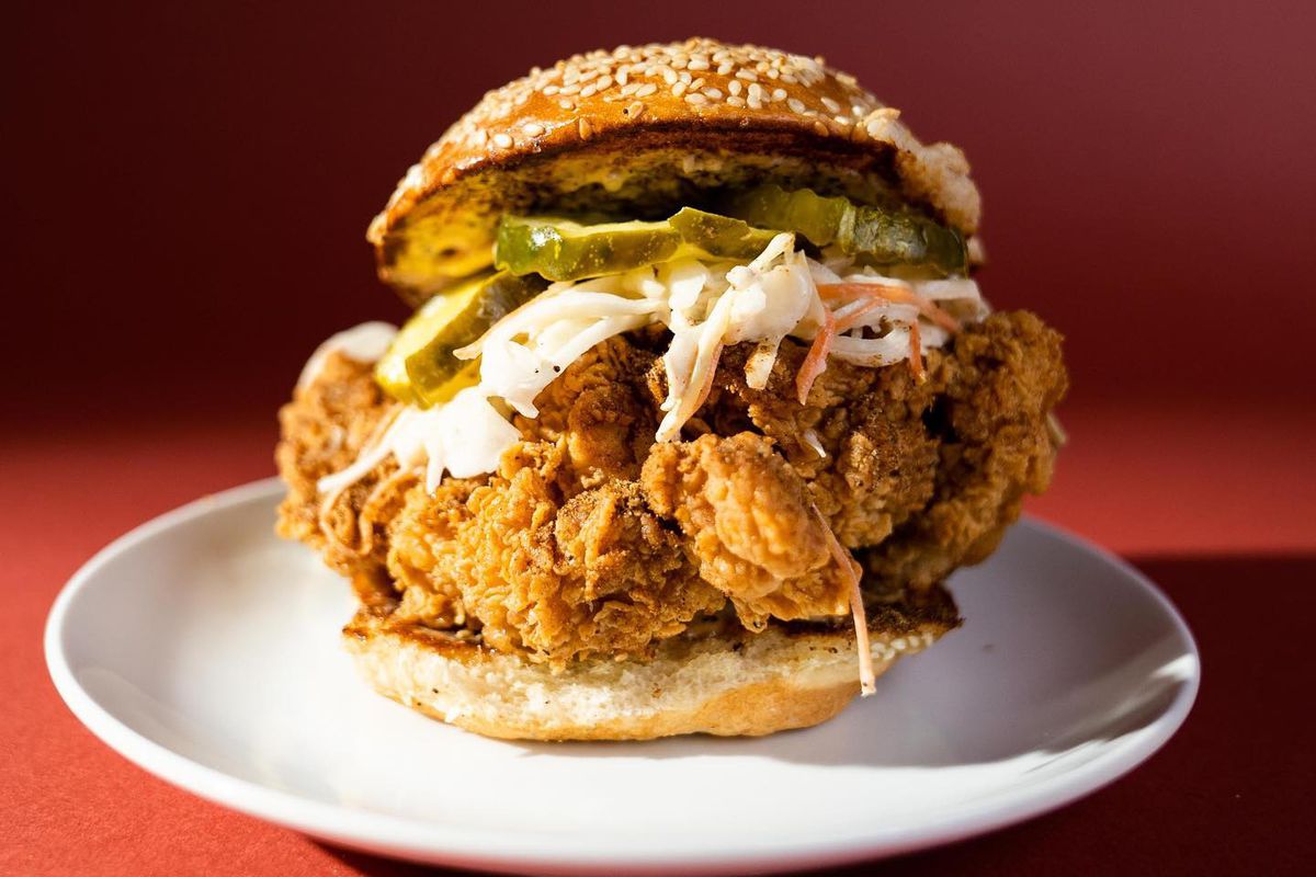 A large fried chicken sandwich with pickles on a white plate