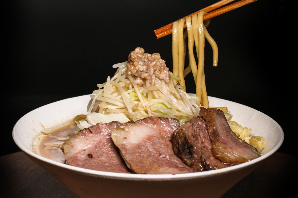 A bowl of wagyu jiro on a black background with chopsticks executing a noodle pull