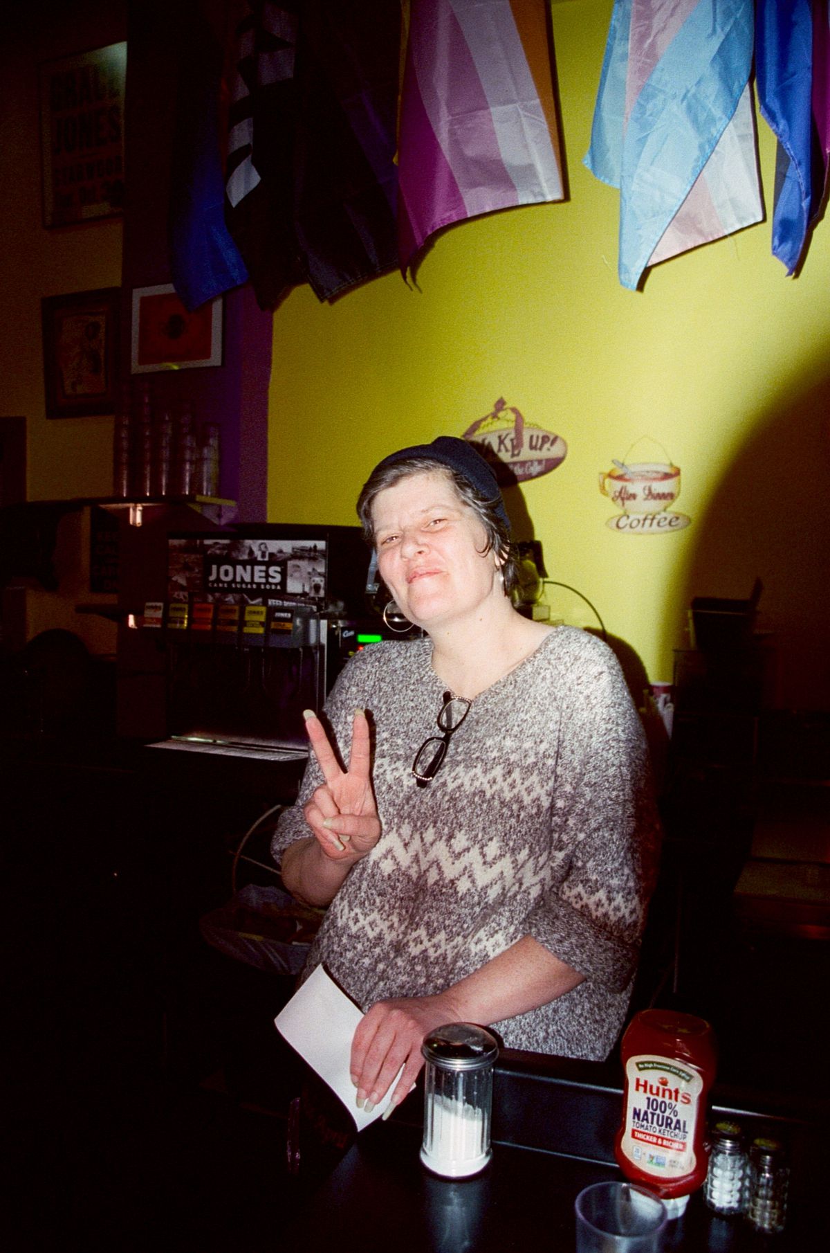 A person with short wavy hair flashes a peace sign, sitting at the counter at the Roxy.