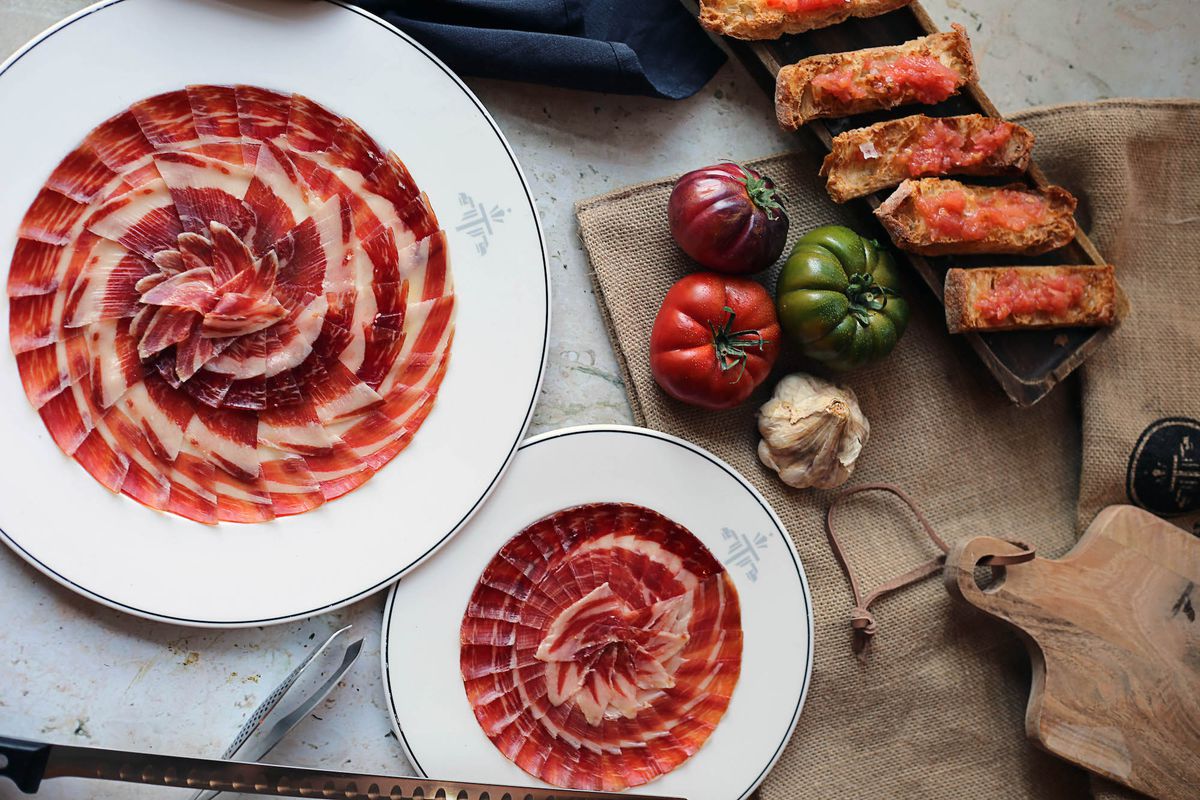An overhead shot of fanned Spanish ham and other Spanish food on a marble table.
