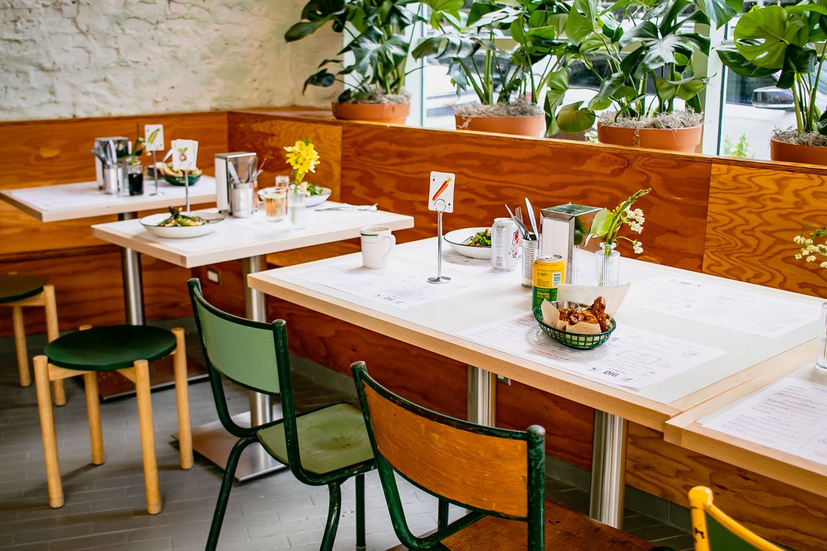 A dining room with a light wooden banquette, tables, and green and orange chairs and stools.