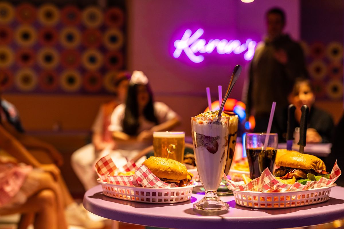 A table laden with American diner food — burgers in baskets and milkshakes