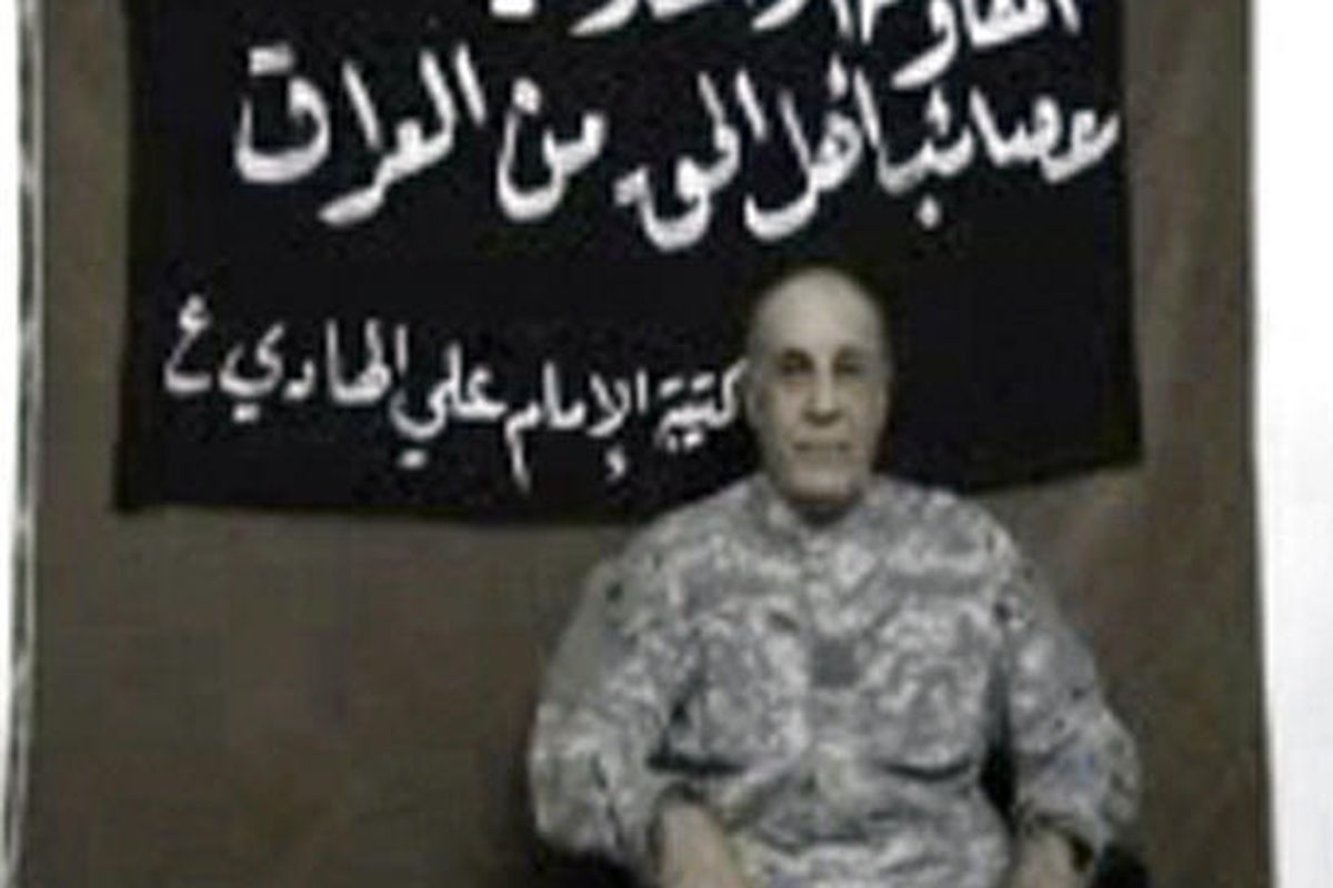 In this undated image made from a video posted on a militant website, a man believed to be missing civilian contractor Issa T. Salomi is seen in front of a banner reading Asaib Ahl al-Haq, or League of the Righteous, Imam Ali regiment. 