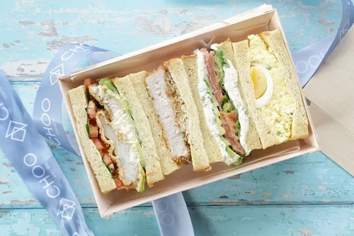 A box of four kinds of Japanese sandwiches on a blue table with ribbon next to it that says Choo Sando
