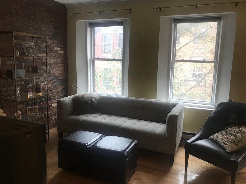 A living room with a couch facing two ottomans, and there are two windows behind the couch.