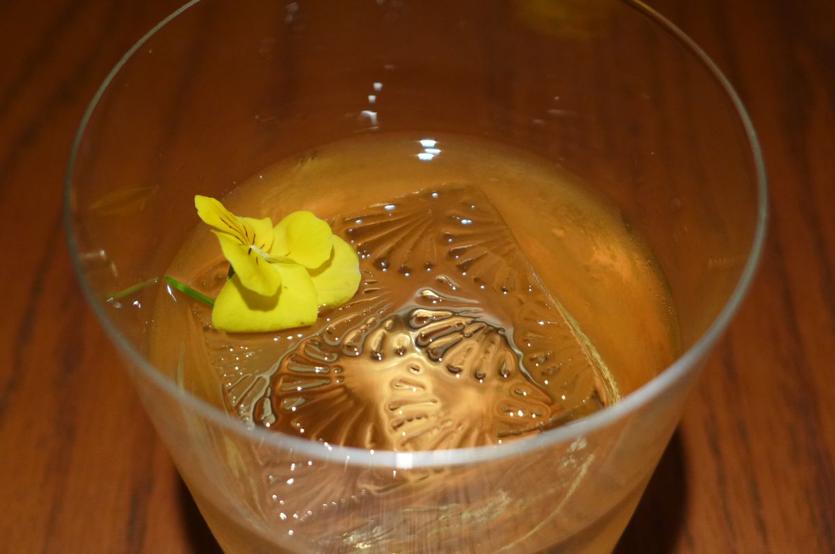 A tumbler seen from above with a patterned ice cube and small yellow flower.