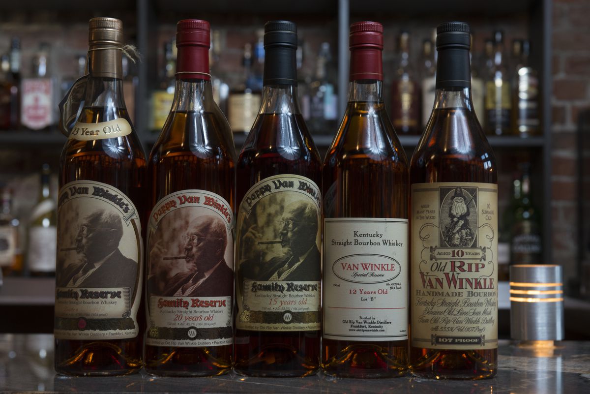 Five different bottles of Pappy Van Winkle, Van Winkle, and Old Rip Van Winkle bourbon sitting on  a bar top with other bottles in the background.