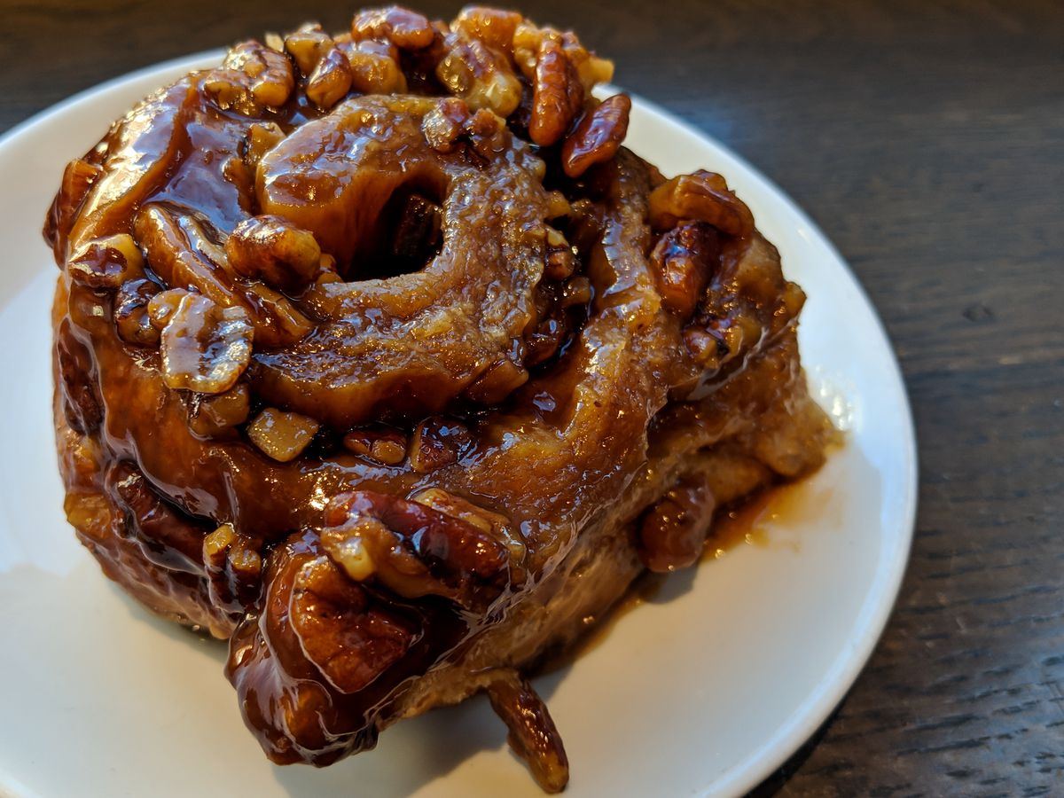A closeup shot of the Flour sticky bun, one of Boston’s iconic dishes, sitting on a white plate on a wooden counter