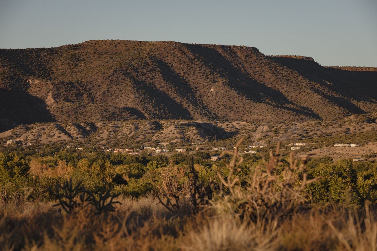 A scattering of small homes dot a desert landscape with a tall mesa in the background.
