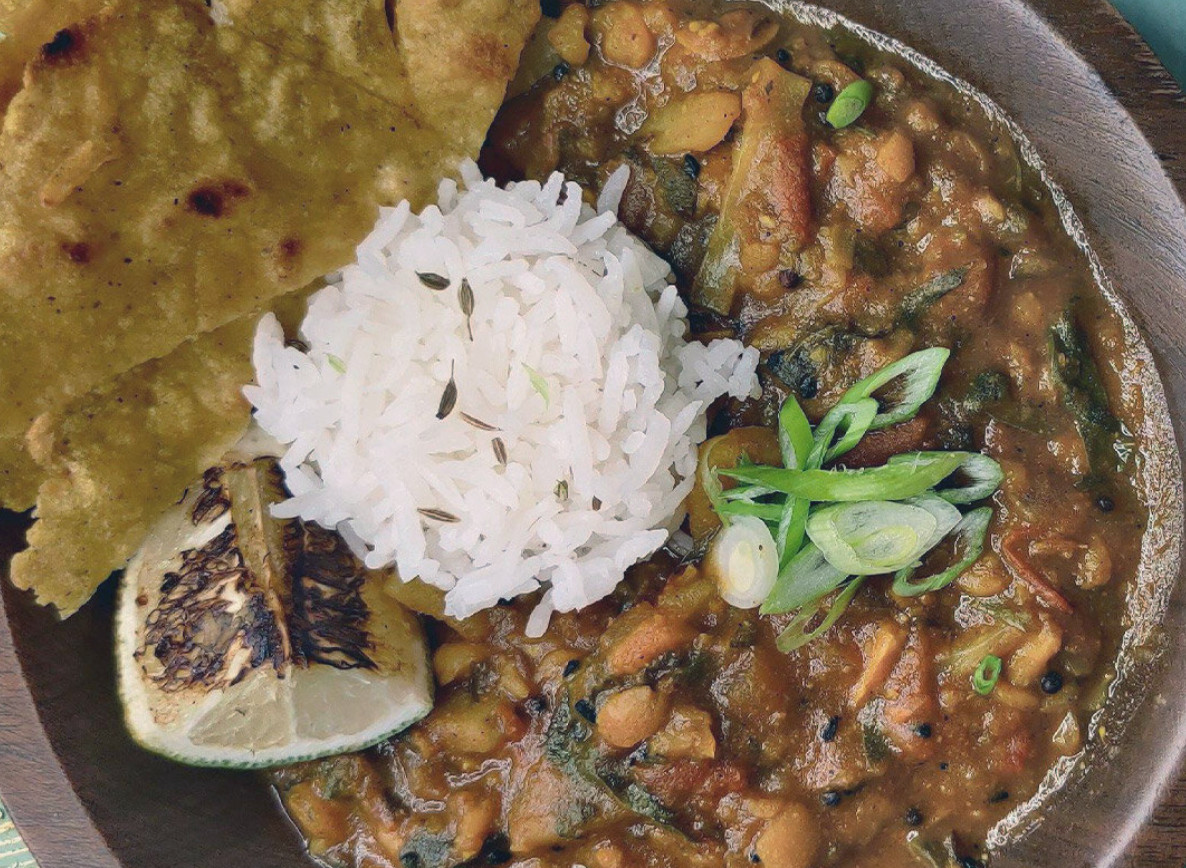 Black-eyed pea masala with a scoop of jeera rice in the center garnished with green onions, a seared lime, and naan.