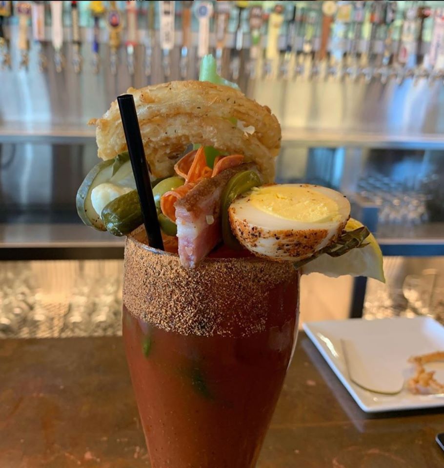 A bloody mary is topped with a variety of toppings, including half a hard boiled egg, fried onion rings, pickles, and more