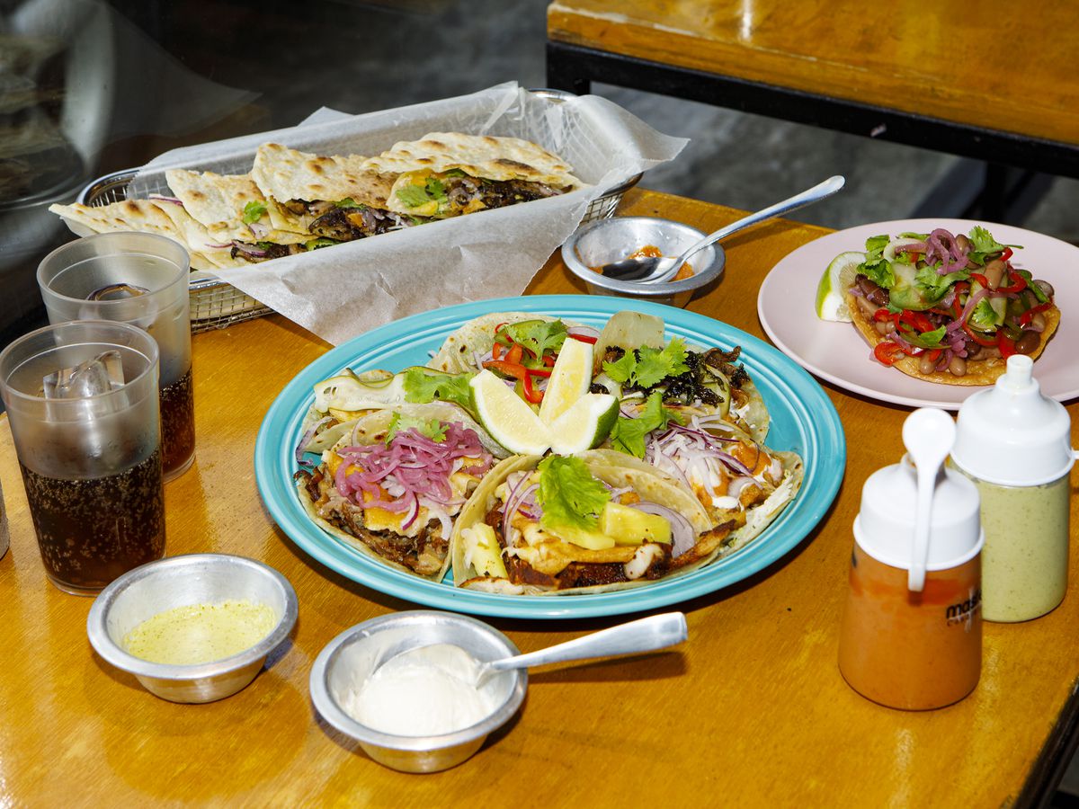A plate of various tacos, on a table alongside quesadillas and other dishes and drinks.