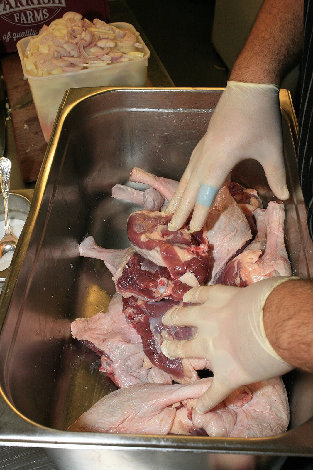 Massaging salt into Barbary duck legs in a metal gastro tray.