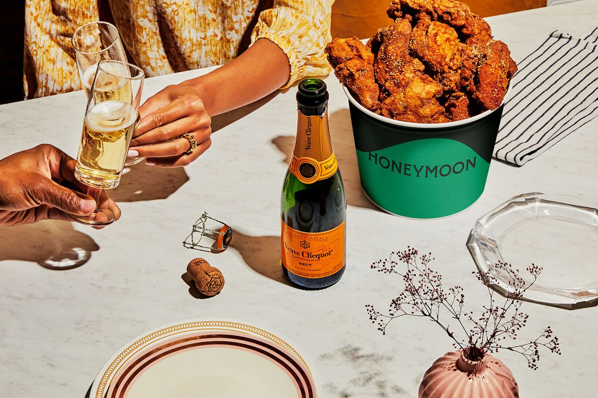 A bottle of Veuve next to a fried chicken bucket  as a customer clinks a glass
