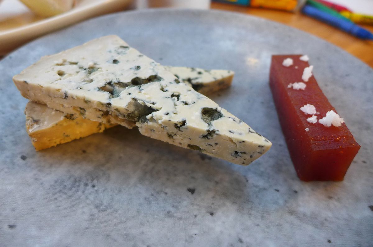 Two wedges of blue cheese angled on top of each other with a plank of dark orange membranillo on the side.