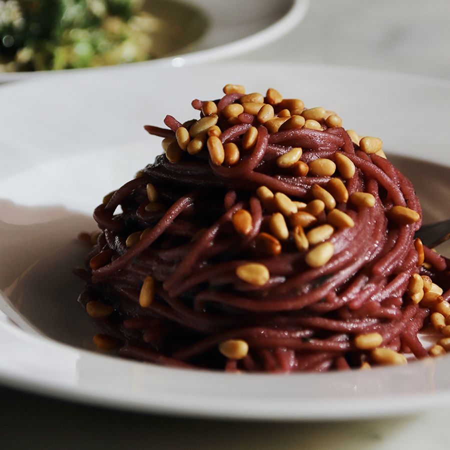 Dark red spaghetti topped with seeds in a white dish. 