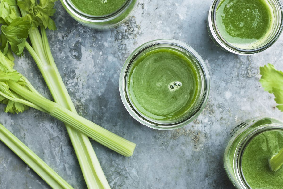 Stalks of celery sit next to glasses full of bright-green celery smoothies.