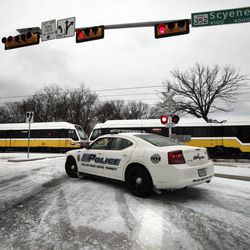 A Dallas Area Rapid Transit police car  blocks a track crossing as a DART light rail train sits motionless along Scyene Road Tuesday, Feb. 1, 2011.  For the first time, DART was forced to close the entire light rail system as a result of severe weather.