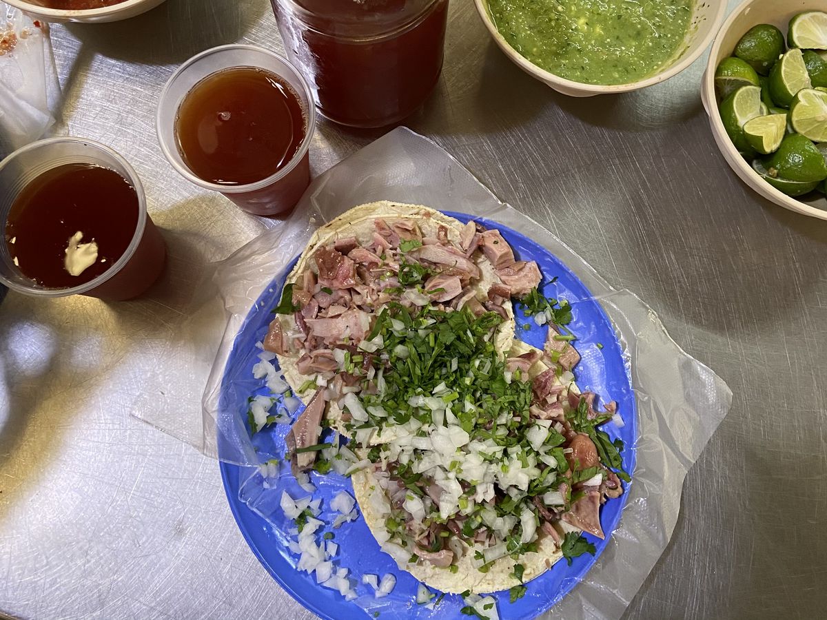 From above, two tacos well covered in cilantro and onions, on a blue plate beside salsas, lime wedges, and other sauces.