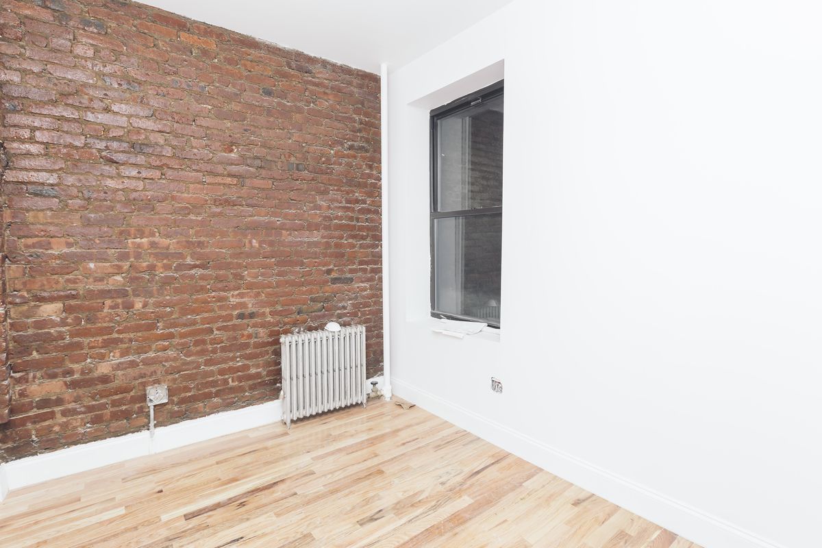 A bedroom with exposed brick, a window, and white walls.