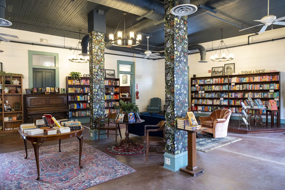 A large bookstore with floral wallpaper columns, dark brown bookshelves filled with books, rugs on the floor, and cozy sofas.