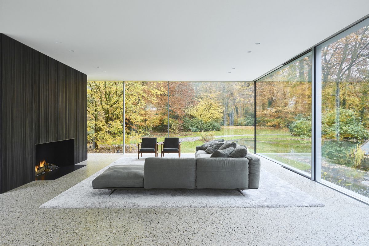 Living room with neutral colors and large windows showing trees going through foliage. 