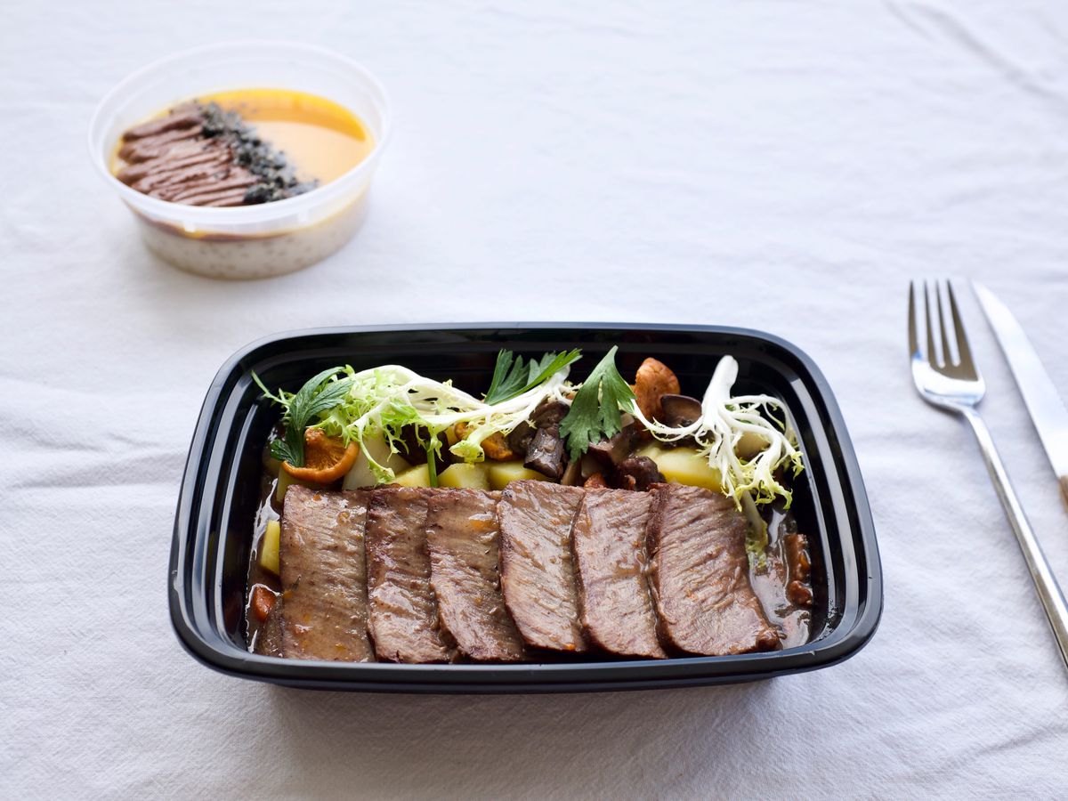 A meaty entree in a takeout container with side salad