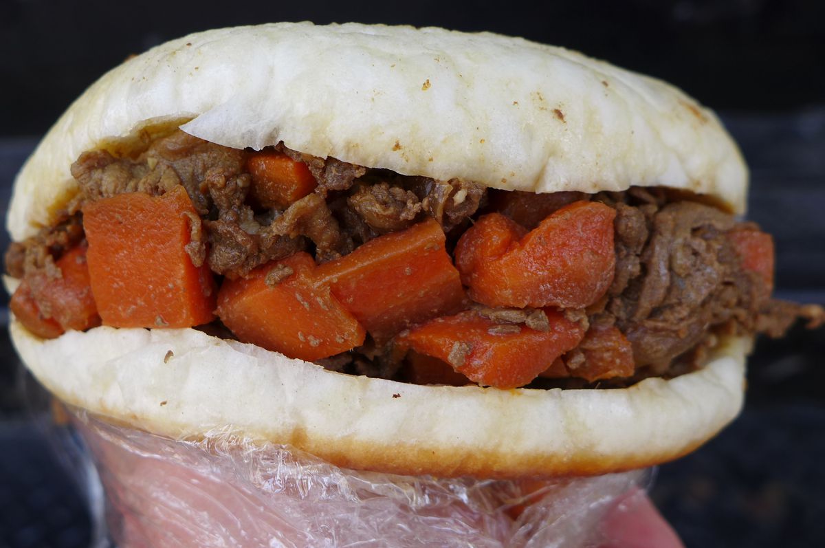 A pita with meat and orange carrot cubes held up.