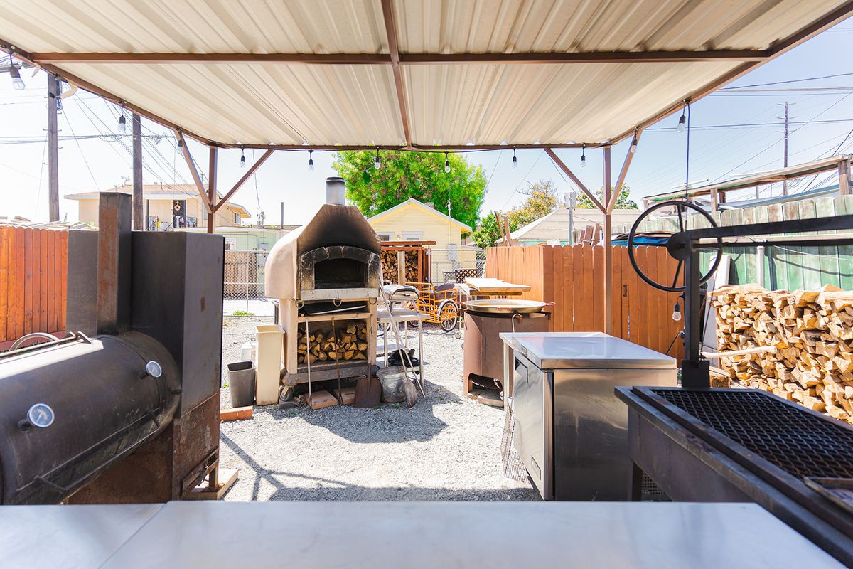 A pizza oven with stacks of wood nearby along with other outdoor kitchen equipment.