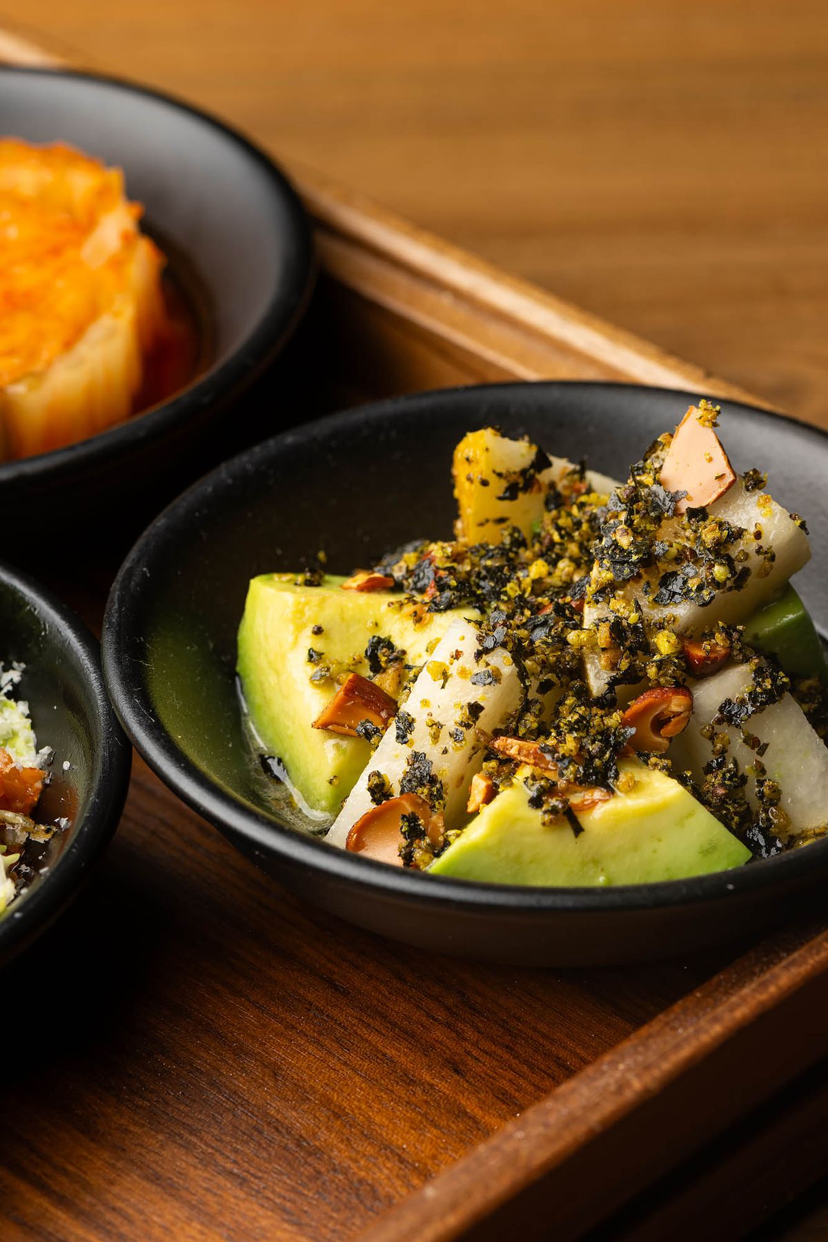 A close up shot of dark black bowl with cuts of pear and avocado as banchan at LA restaurant Yangban.