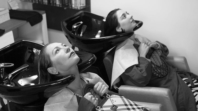 A mother and a daughter sit with their heads in salon hair-washing tubs.