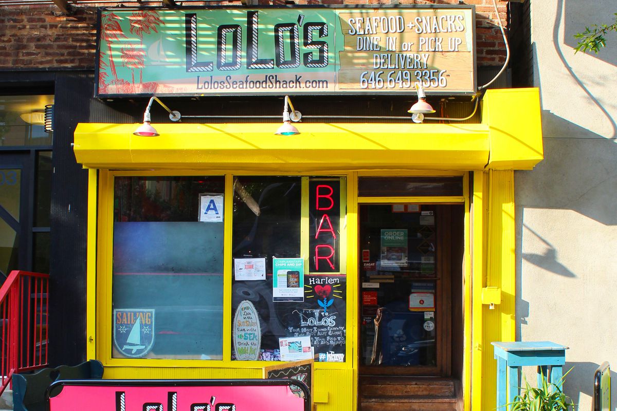 The colorful, pink and yellow storefront of a restaurant advertises takeout and delivery services 