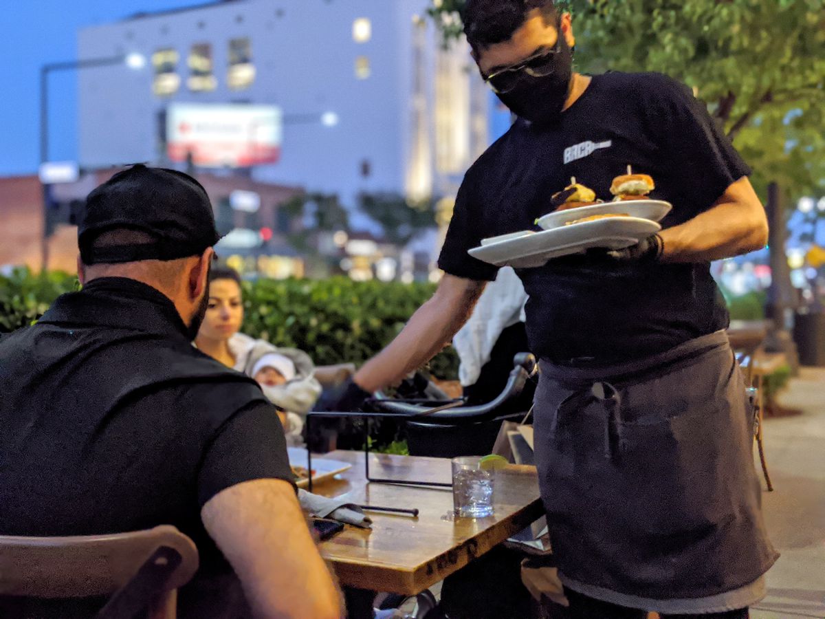 Server places dishes at an outdoor dining table in Glendale, CA