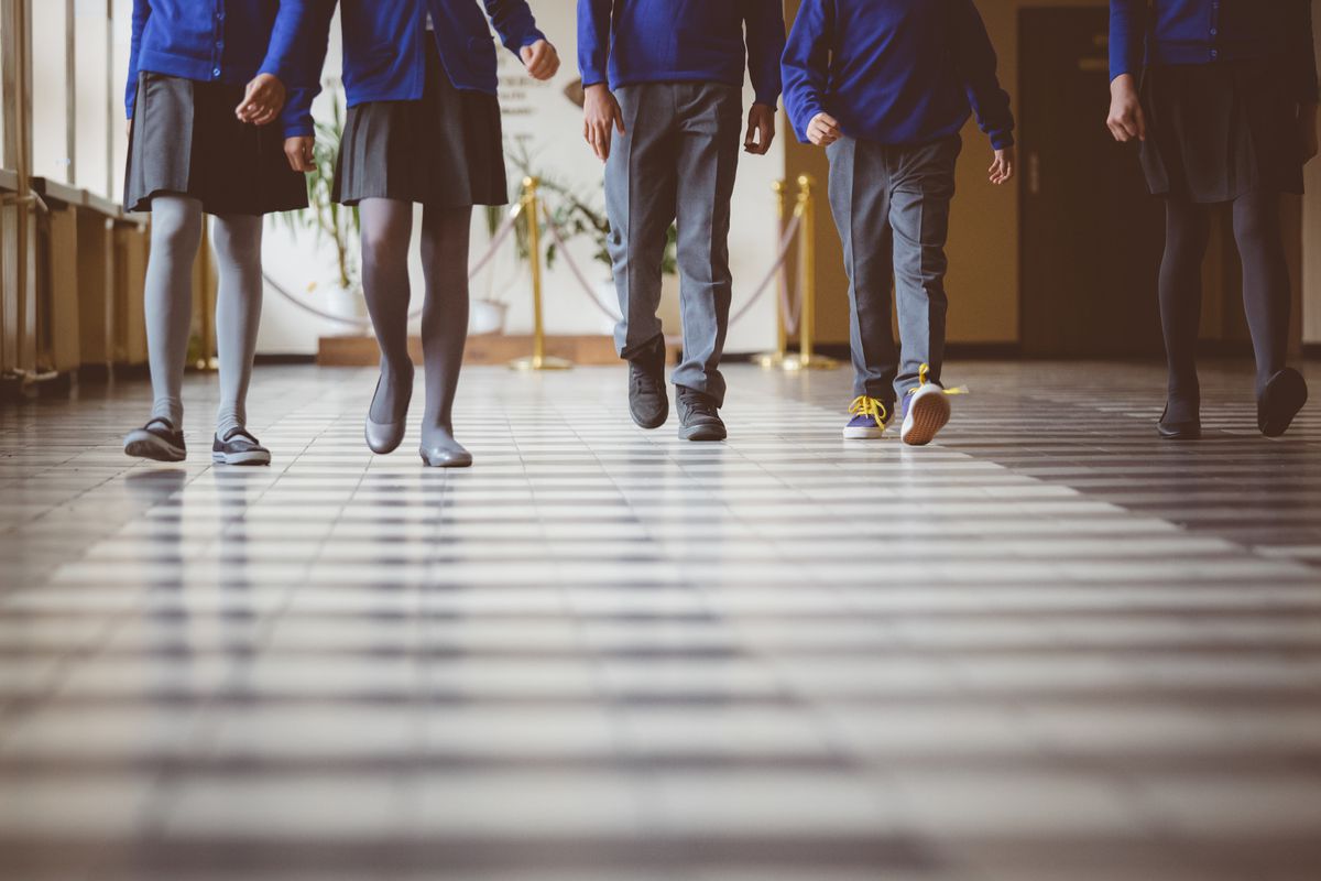 Cropped image of school kids in uniform walking together in a row through corridor. 