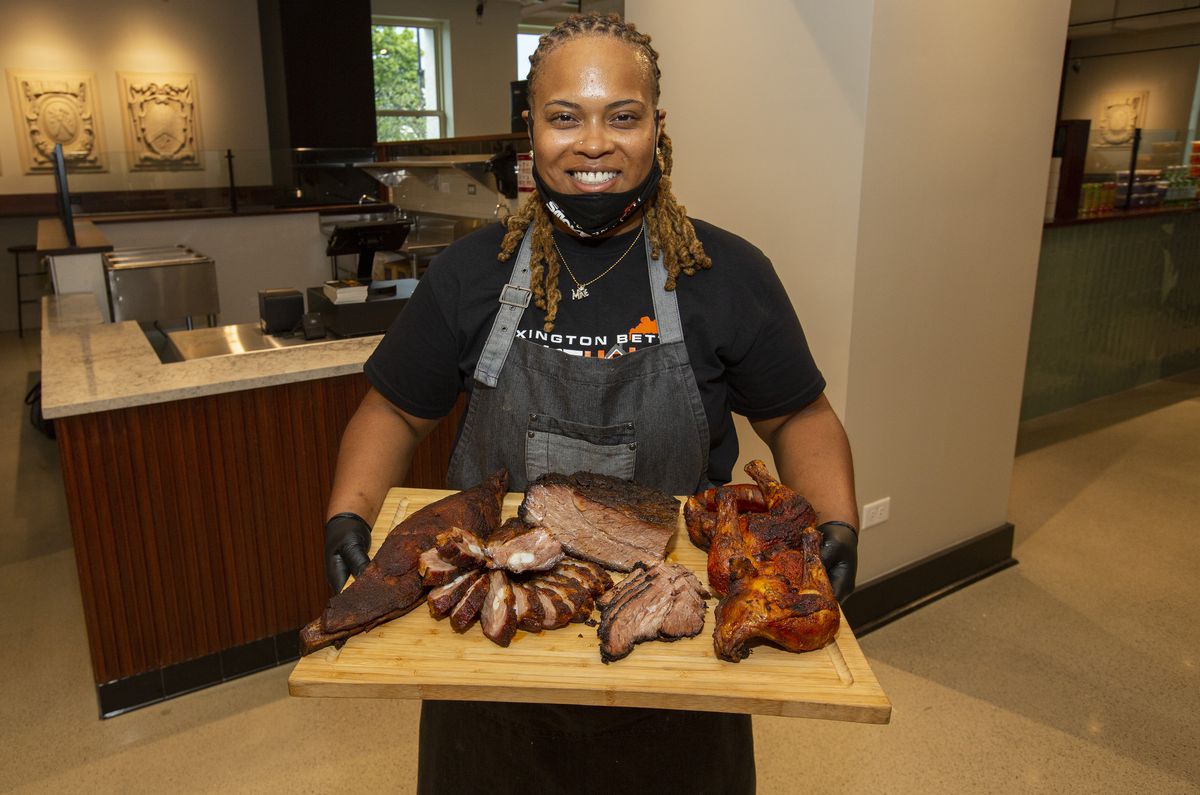 A female chef holds a wooden board filled with different kinds of barbecued meats