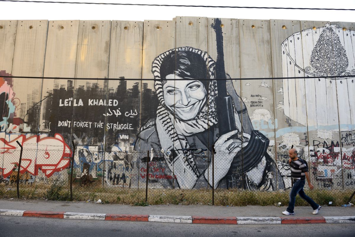 A mural of Leila Khaled’s famous photo, in which she is wearing a keffiyeh like a headscarf while holding a rifle, graffitied on the West Bank wall