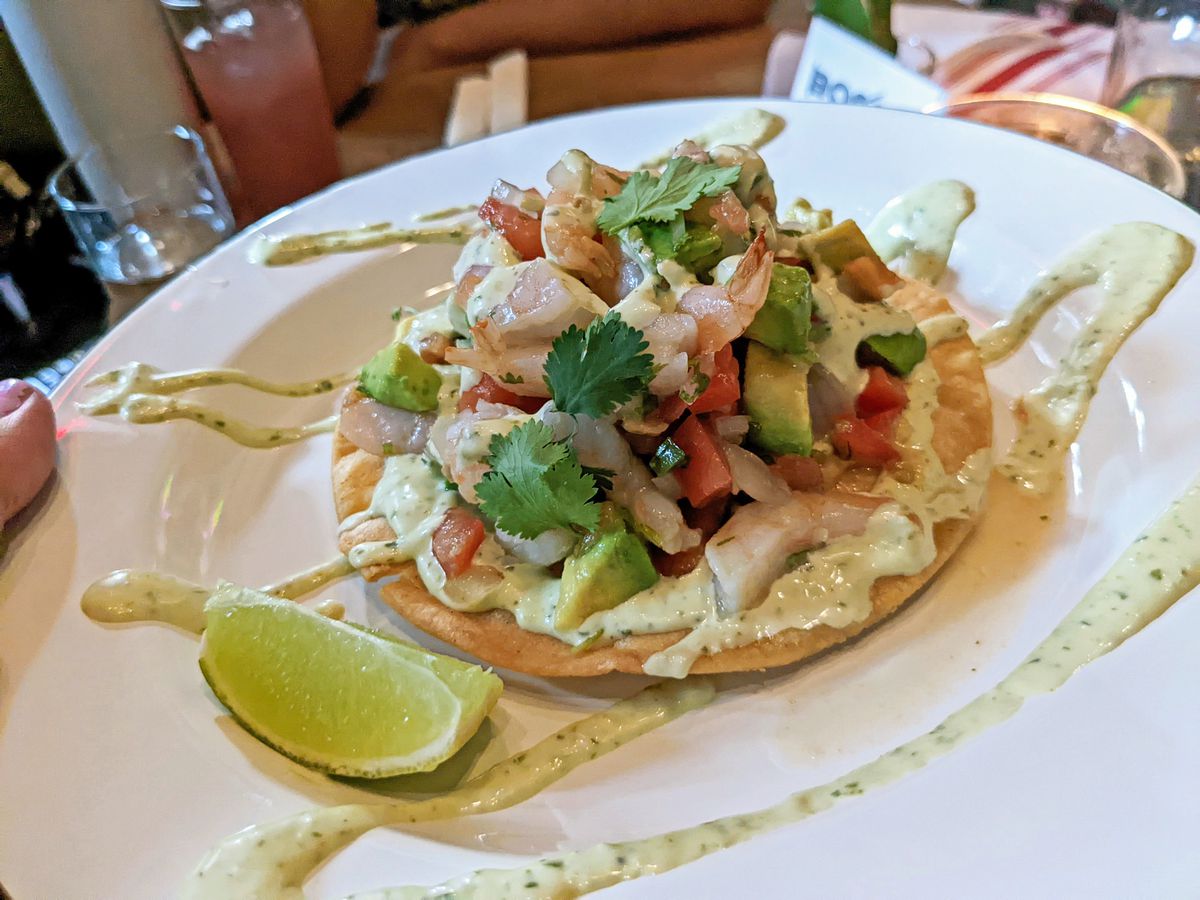 A flat hard tortilla with ceviche piled high on top and squiggled with massive amounts of green mayo.