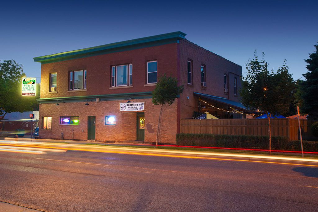 The exterior of Skinner’s Pub, a brick building on a road at dusk with a glowing sign. 